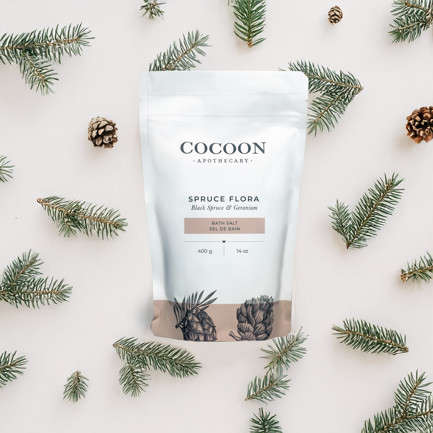 Cocoon Apothecary Spruce Flora bath salt packaging surrounded by black spruce branches on a light background