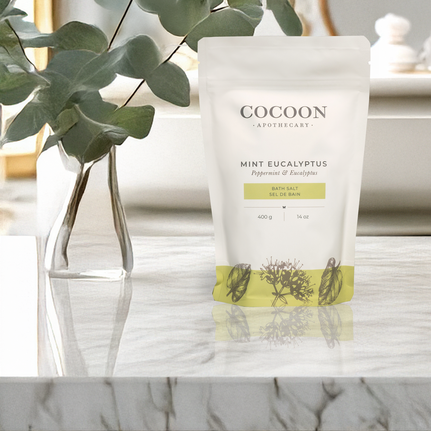 Cocoon Apothecary Mint Eucalyptus bath salt packaging on a marble surface with a plant in the background.