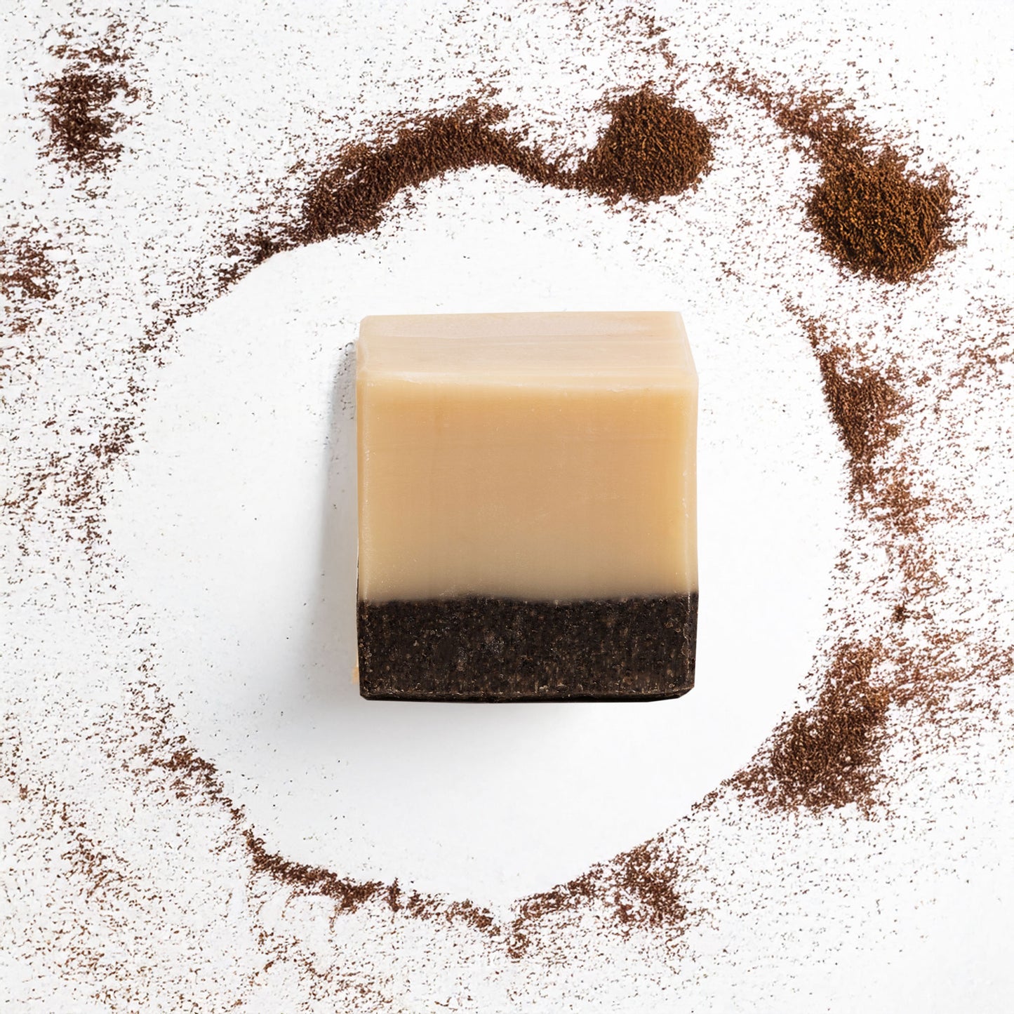 Bar of soap with a layered appearance surrounded by coffee grounds on a white background