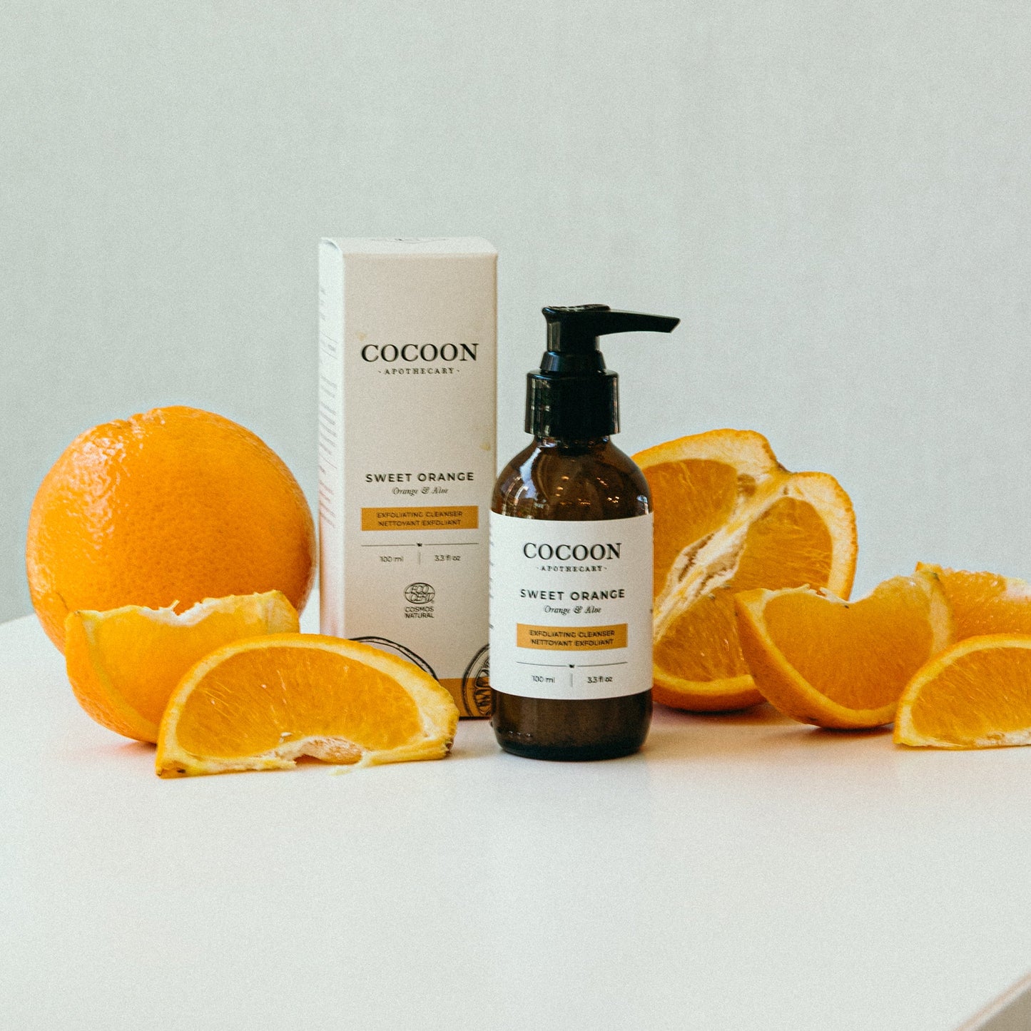 Sweet Orange Exfoliating Cleanser with oranges on a white surface and light green background