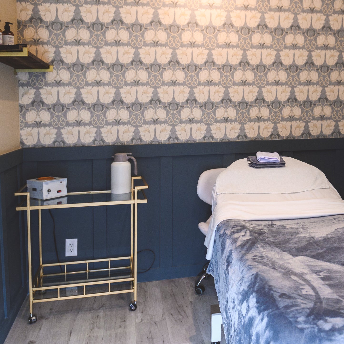 Advanced pedicure room with a bed, cart, and wall decor.
