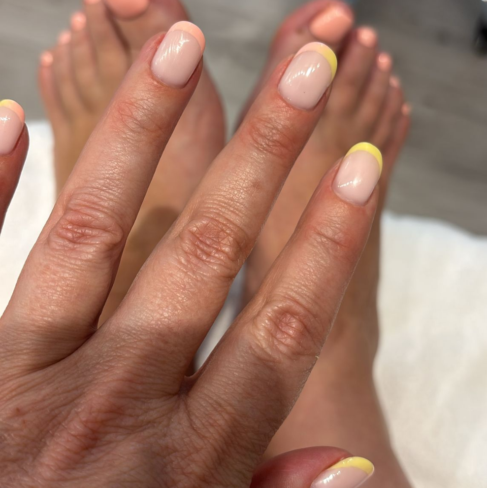 Close-up of hands with light pink and yellow nail polish on a blurred background