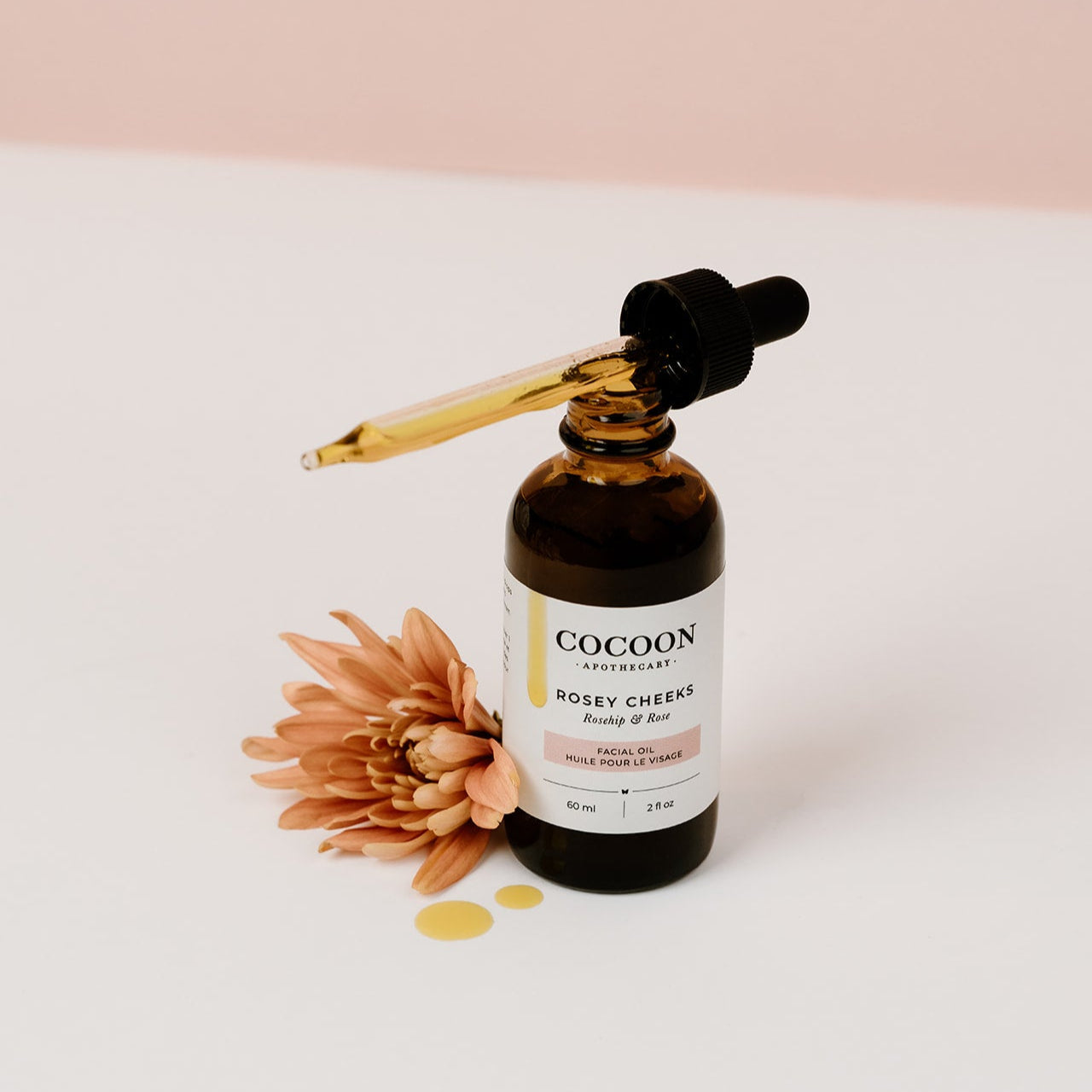 Rosey Cheeks Facial Oil bottle with dropper on a light pink background