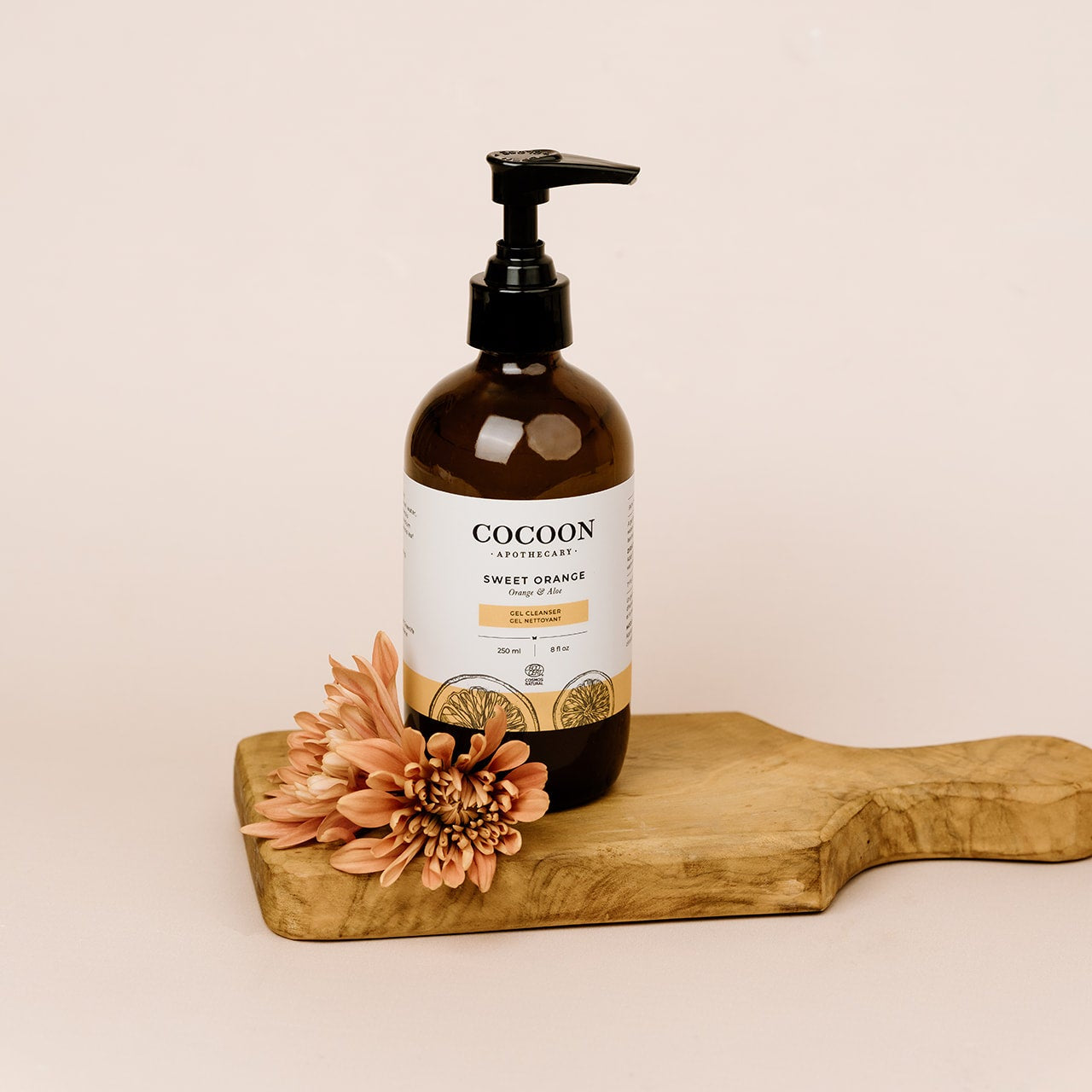 Cocoon Apothecary bottle on a wooden board with a flower on a beige background