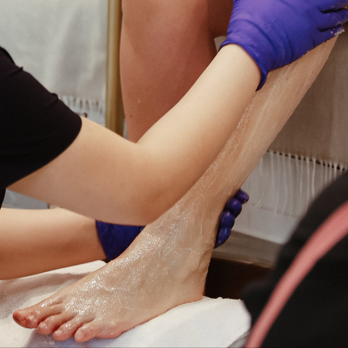 Person receiving a leg treatment in a spa setting with a masked professional.