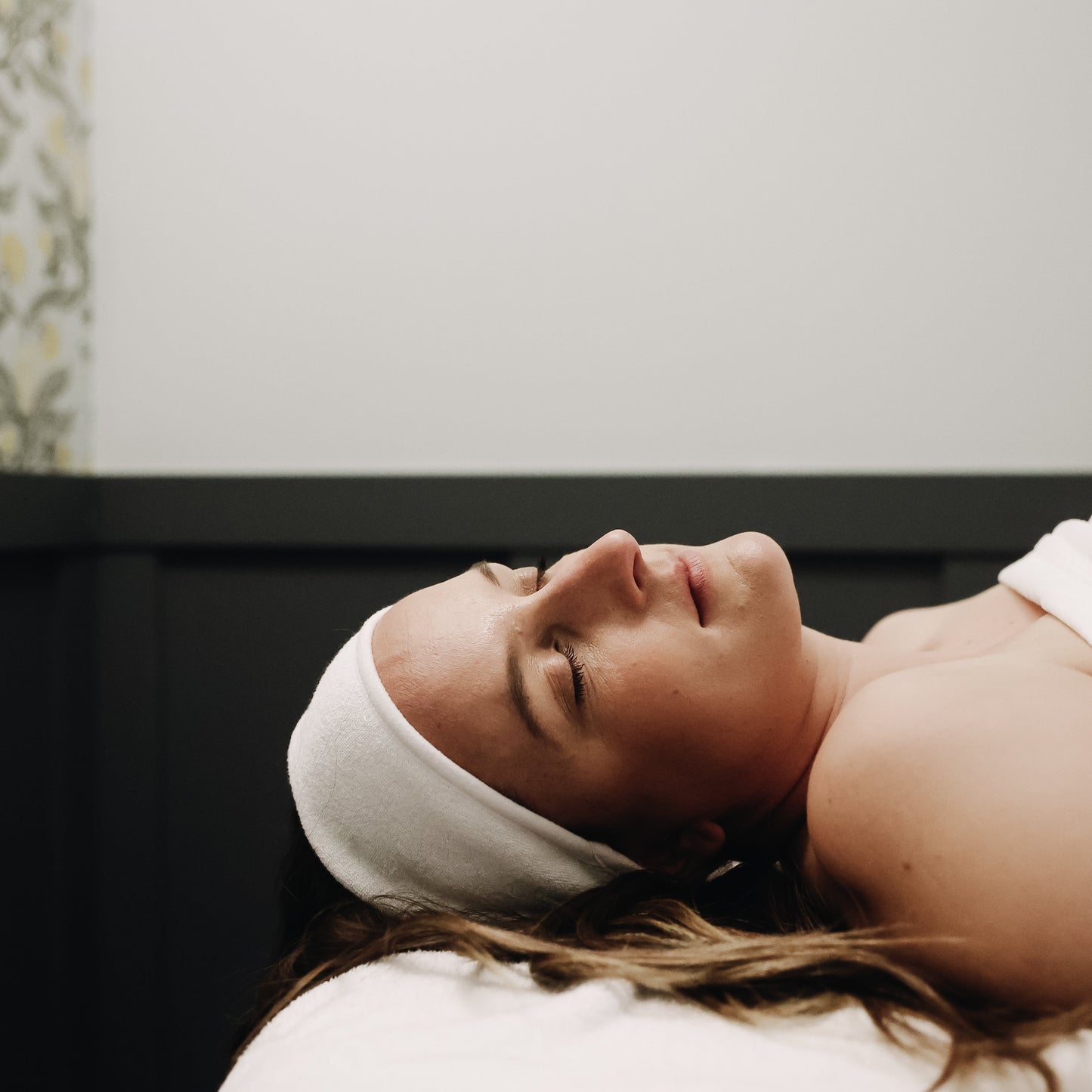 Woman receiving a facial treatment with a headband on, in a spa setting.