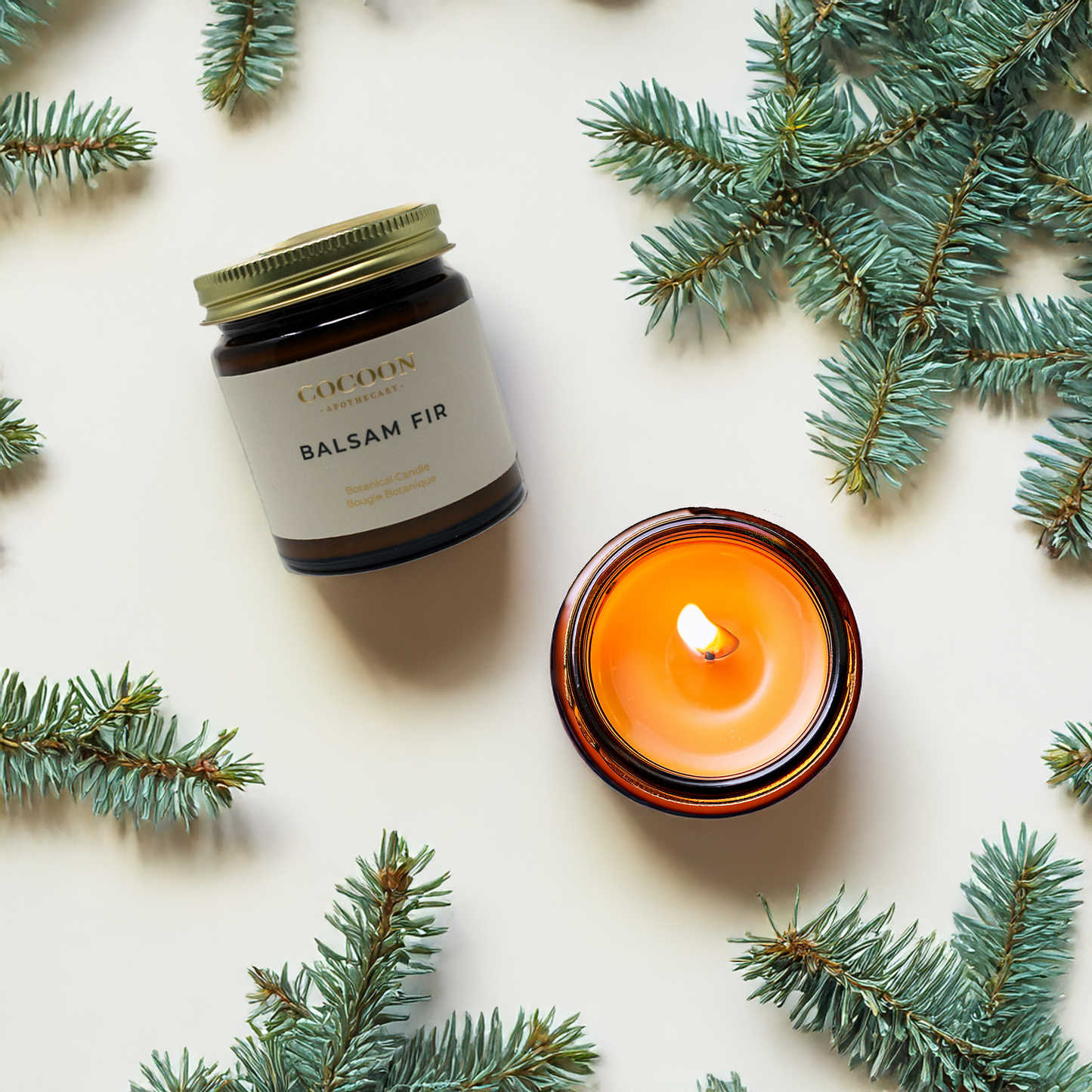 Candle and jar with 'Balsam Fir' label surrounded by pine branches on a light background
