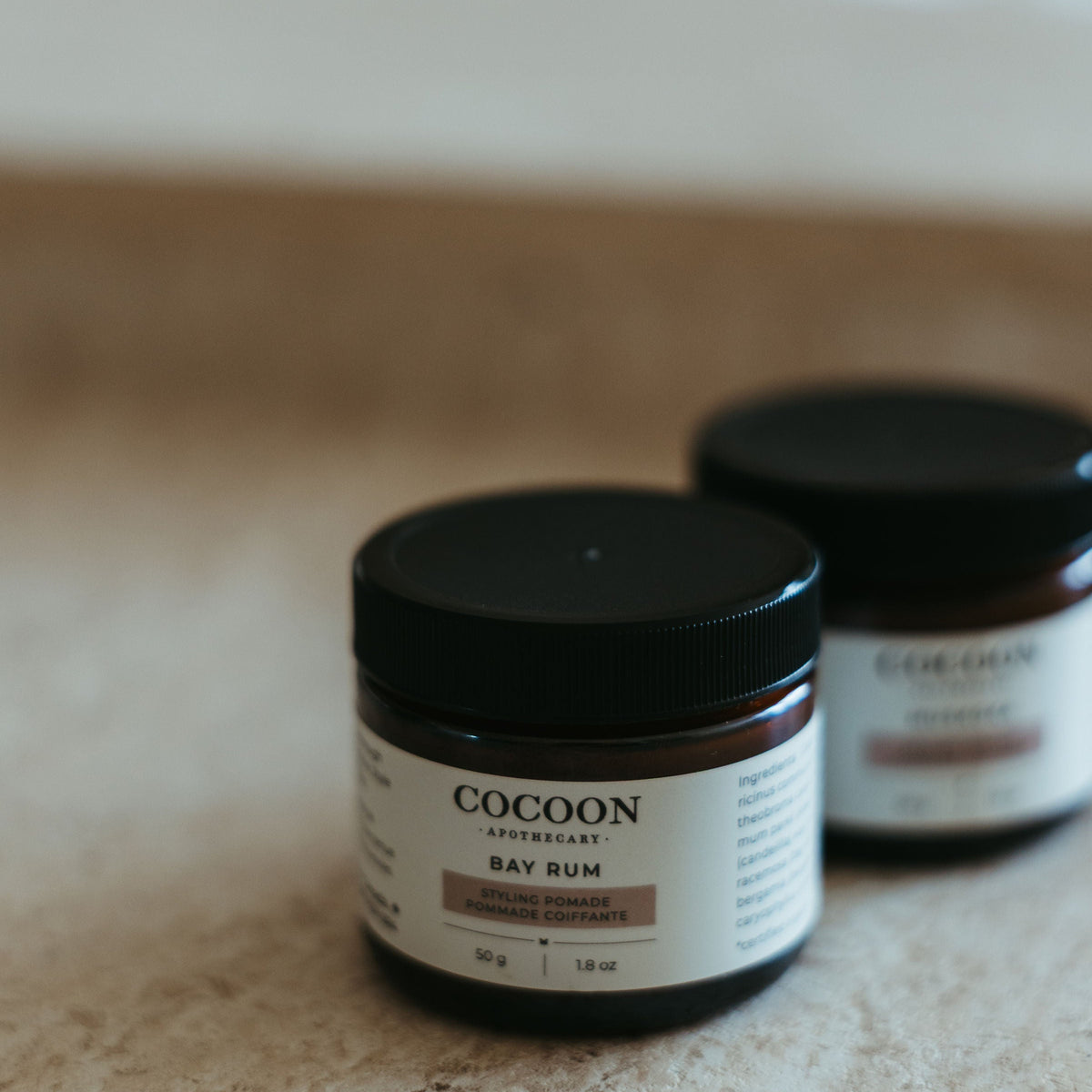 Two jars of Cocoon Bay Rum on a textured surface with a blurred background