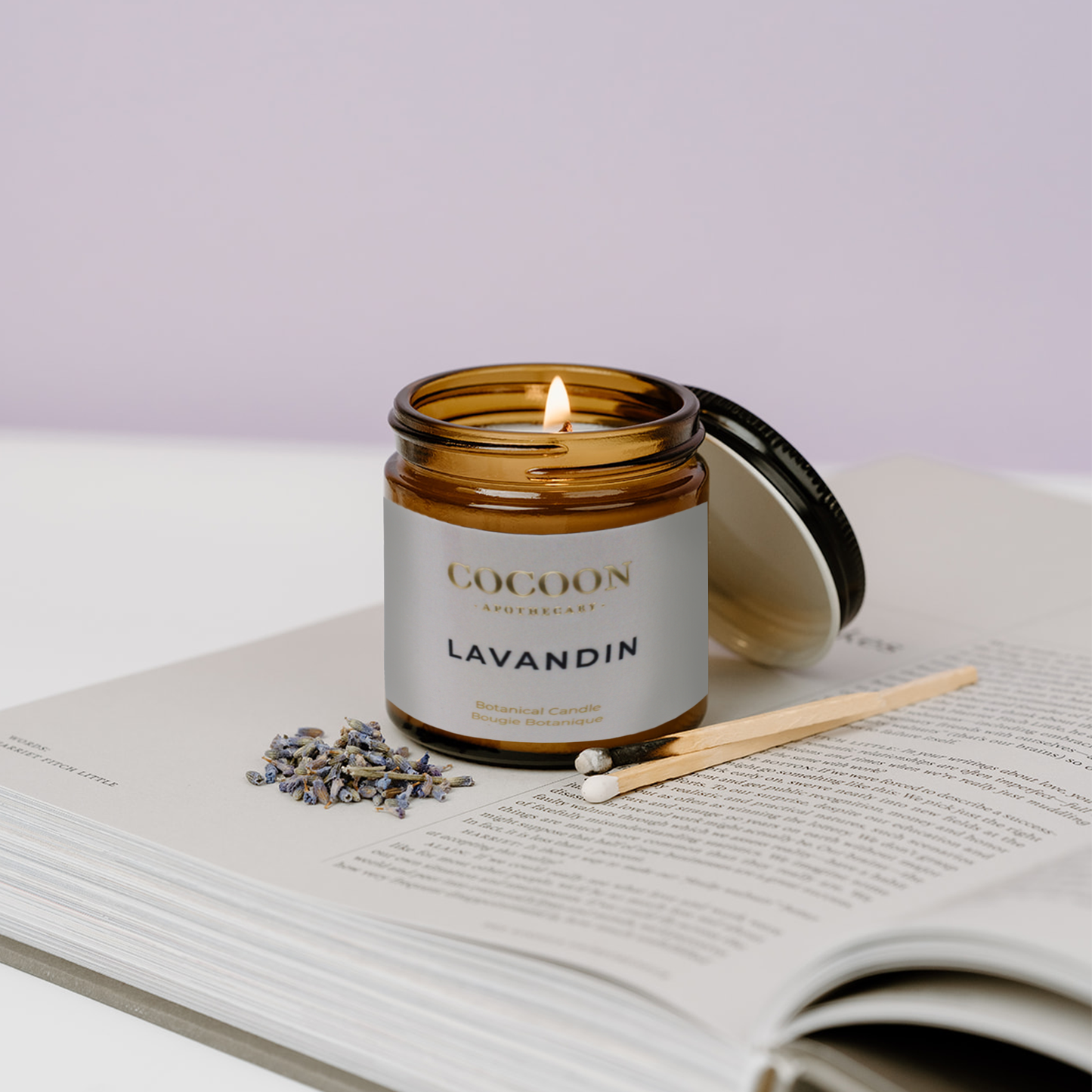 Cocoon Lavandin candle in a brown jar on an open book with lavender flowers.