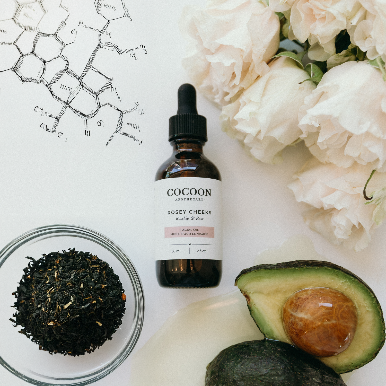 Cocoon Apothecary bottle with avocado, flowers, and tea leaves on a white background