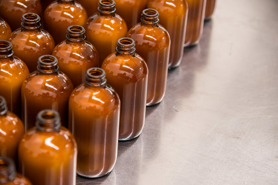 Row of glass bottles filled with a brown liquid on a reflective surface