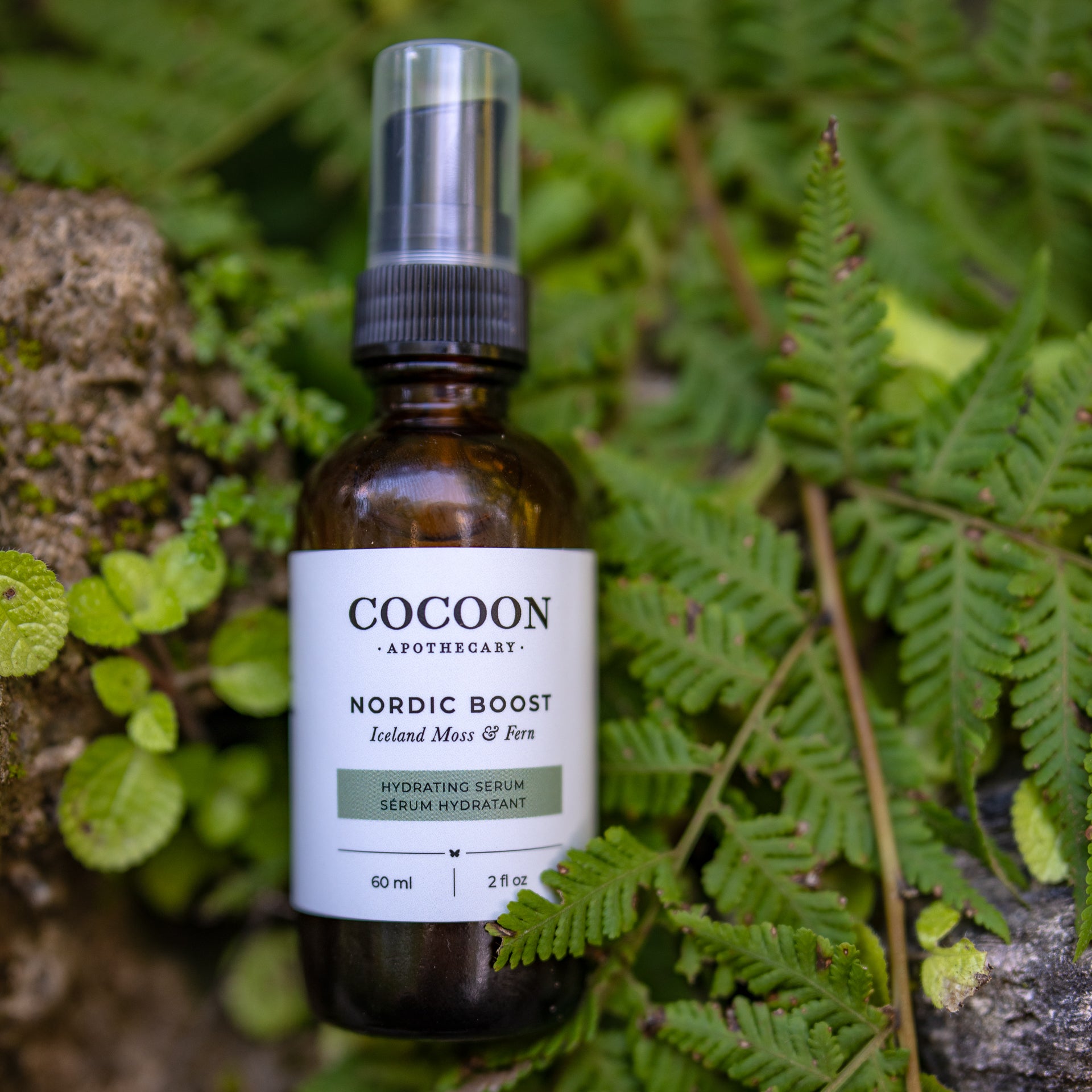Cocoon Apothecary Nordic Boost serum bottle on a natural background with green leaves.