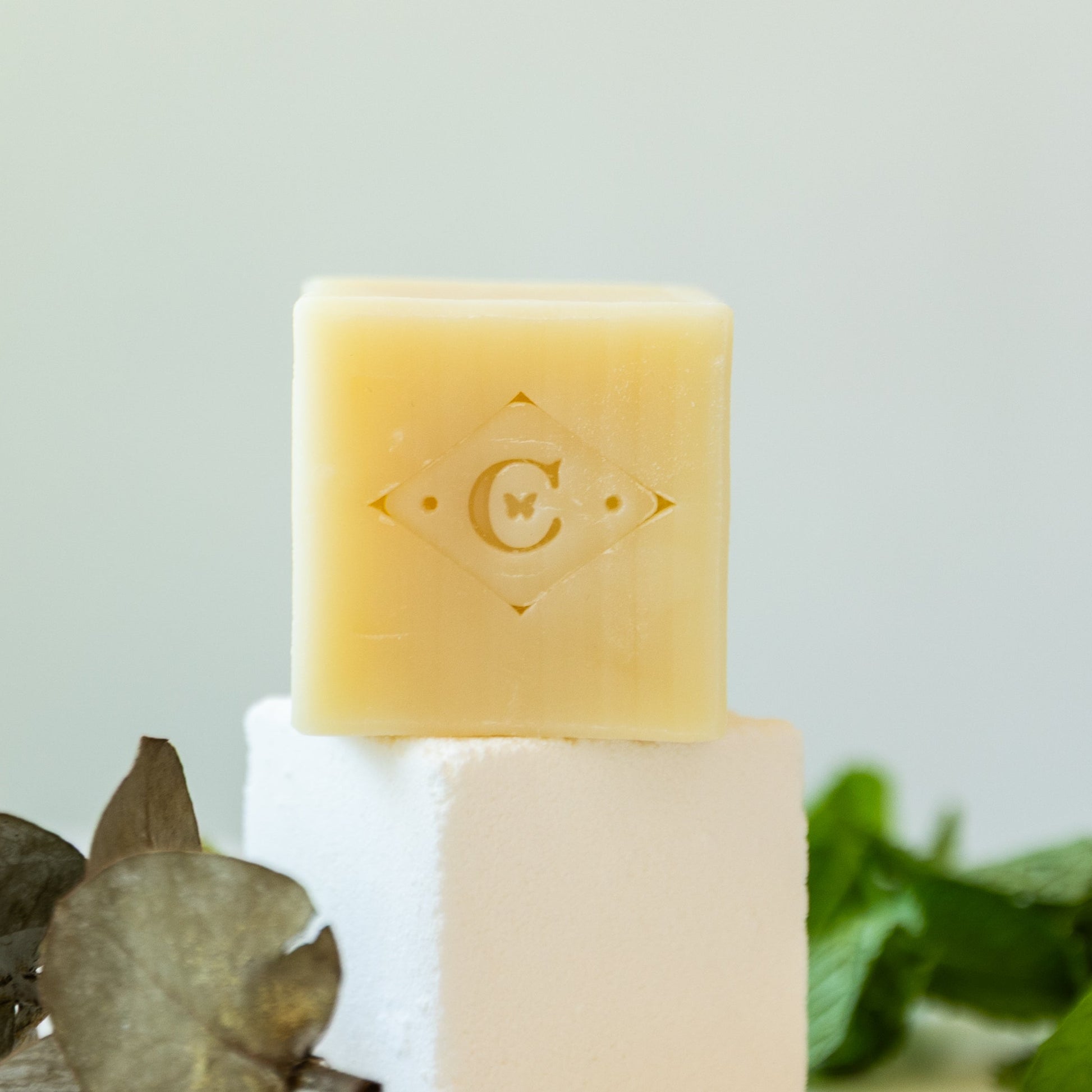 Bar of soap on a white stand with a mint sprigs and eucalyptus