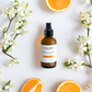Cocoon skincare bottle with orange blossoms and oranges on a light background