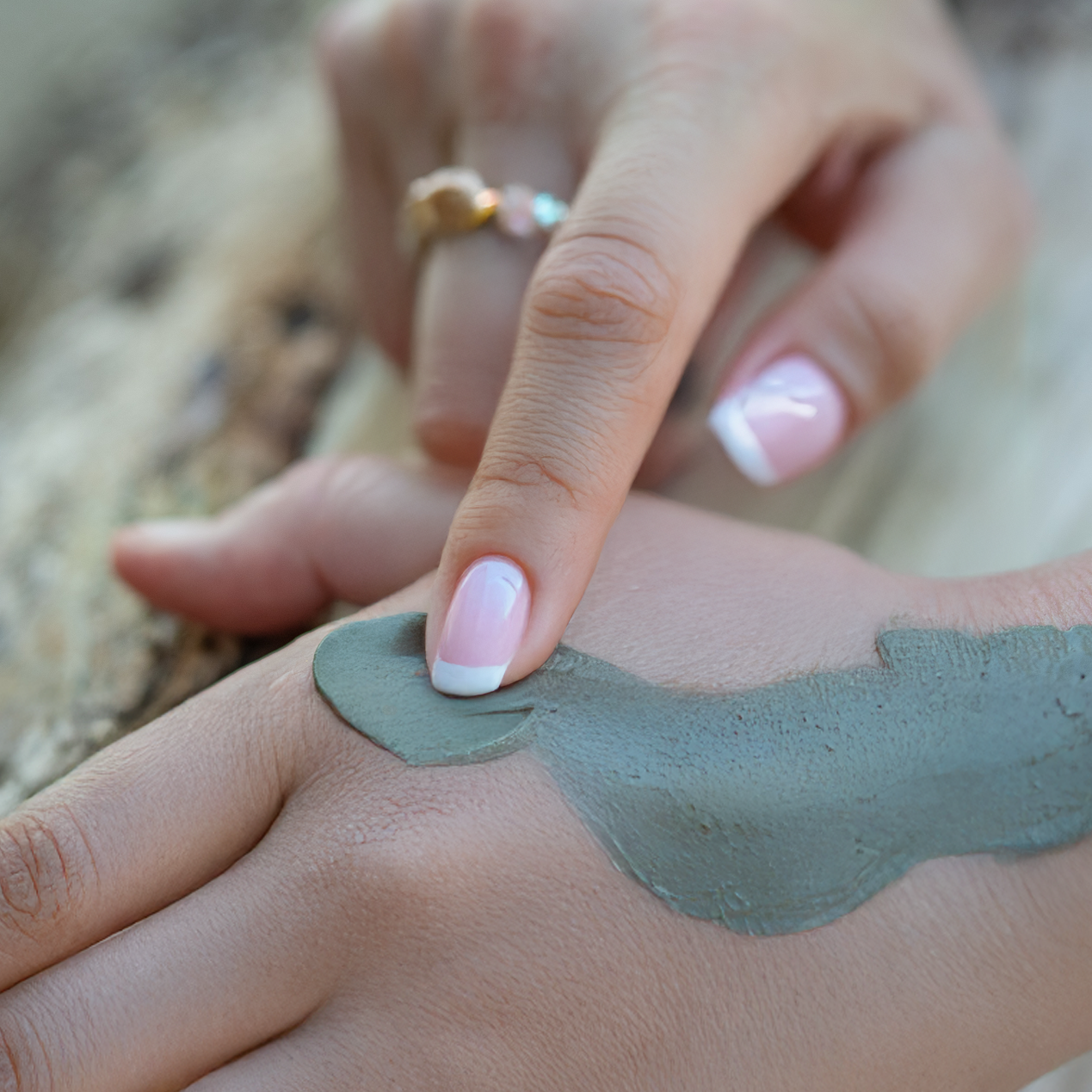 Hand applying a patch of green mud to another hand outdoors.