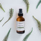 Cocoon Nordic Boost serum bottle surrounded by green leaves on a light background