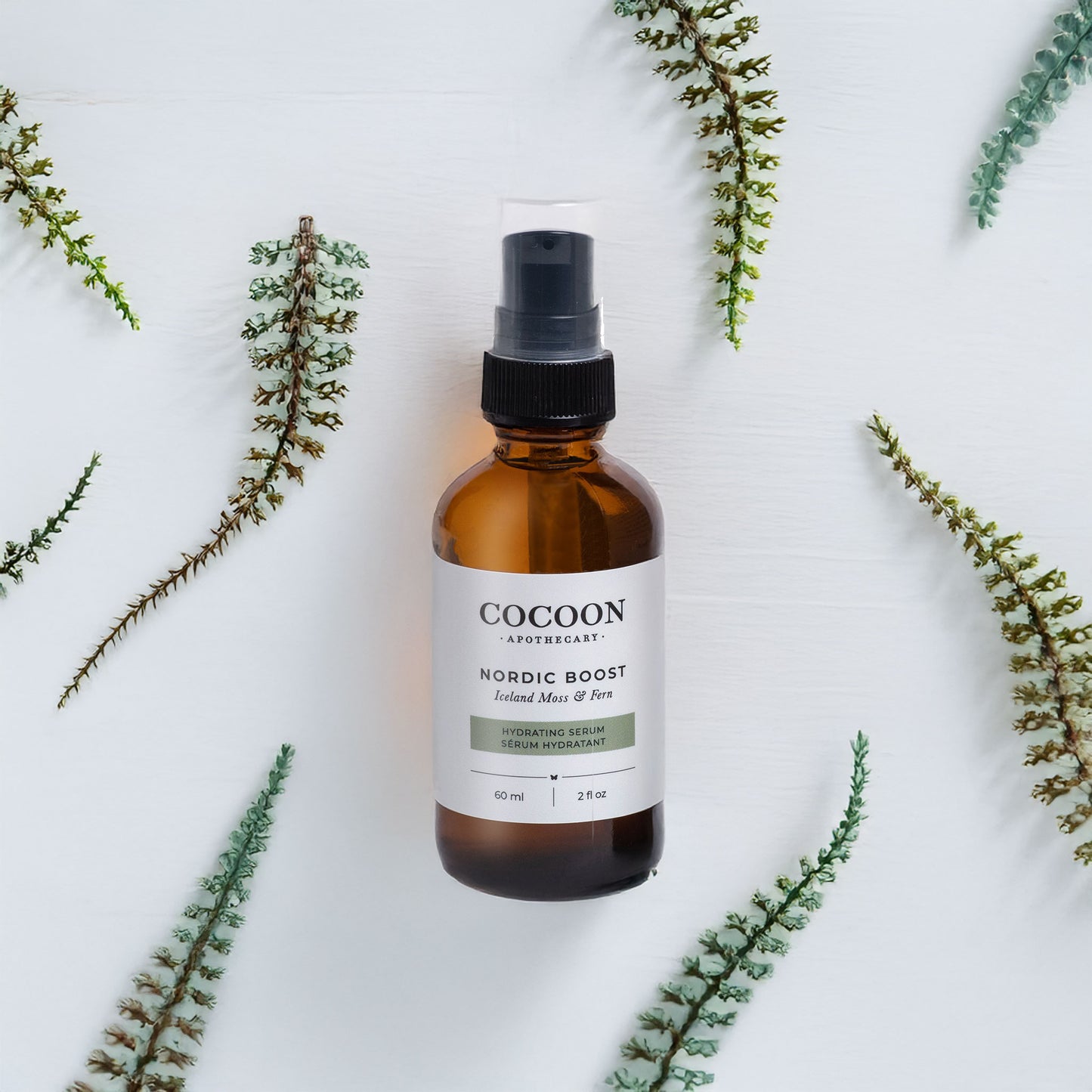 Cocoon Nordic Boost serum bottle surrounded by green leaves on a light background