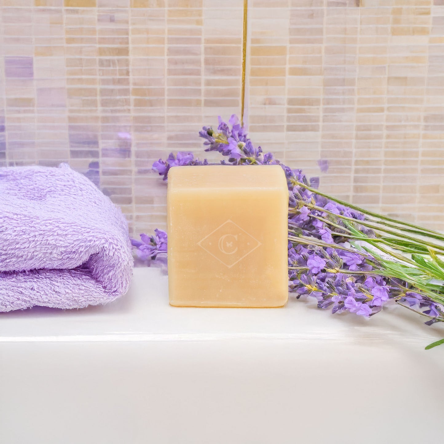 Bar of soap with lavender flowers and a towel on a bathroom counter.