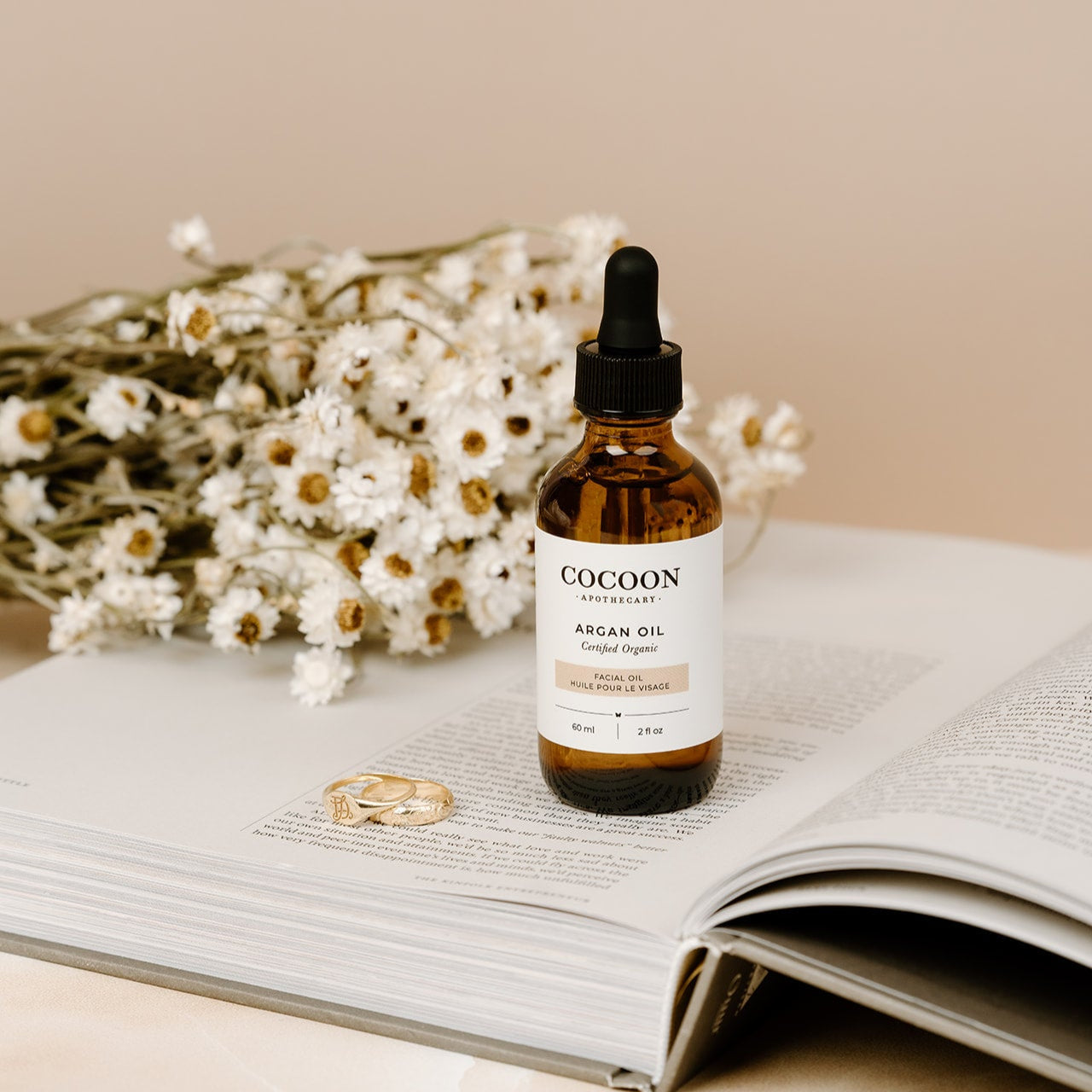 Cocoon Argan Oil bottle on an open book with flowers in the background