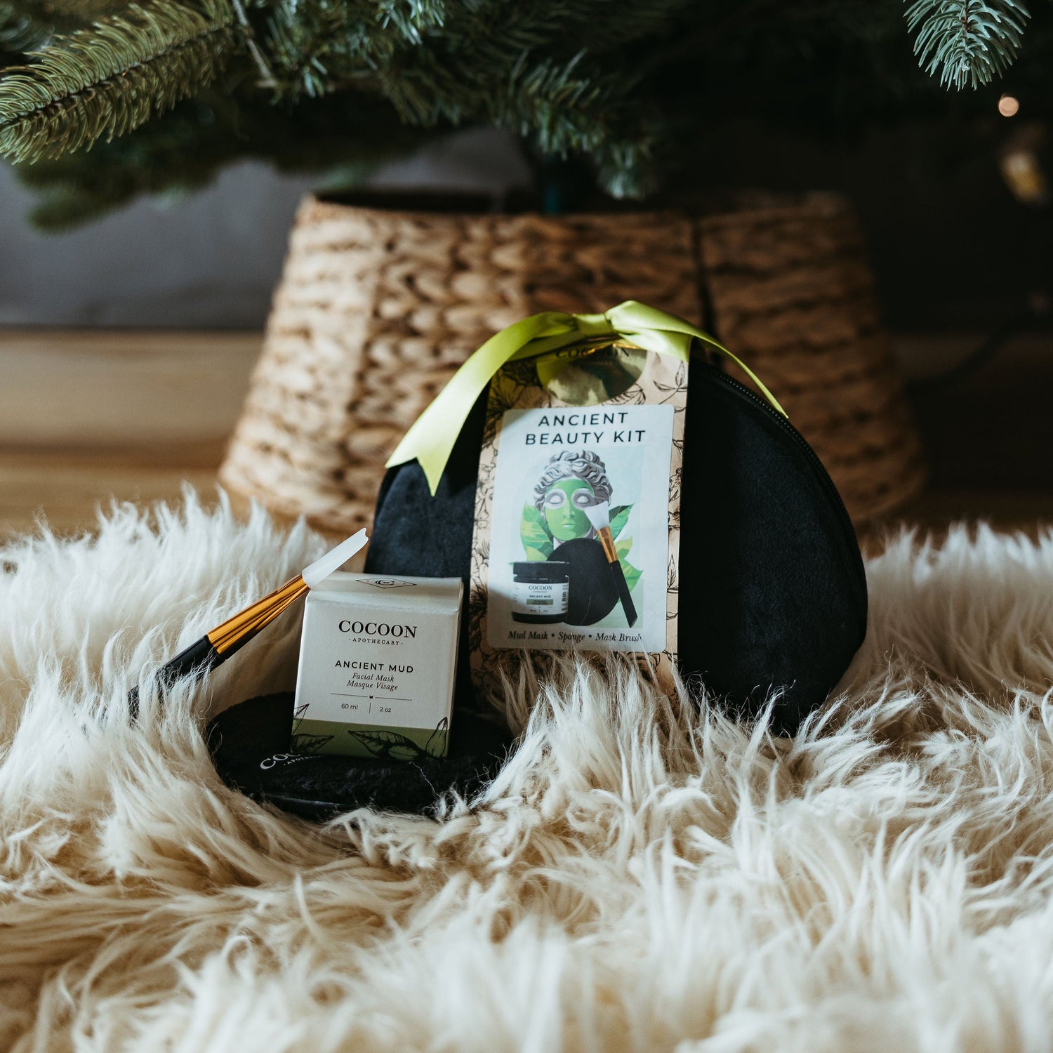 Two bottles of Caudron wine under a decorated Christmas tree on a fluffy white rug.