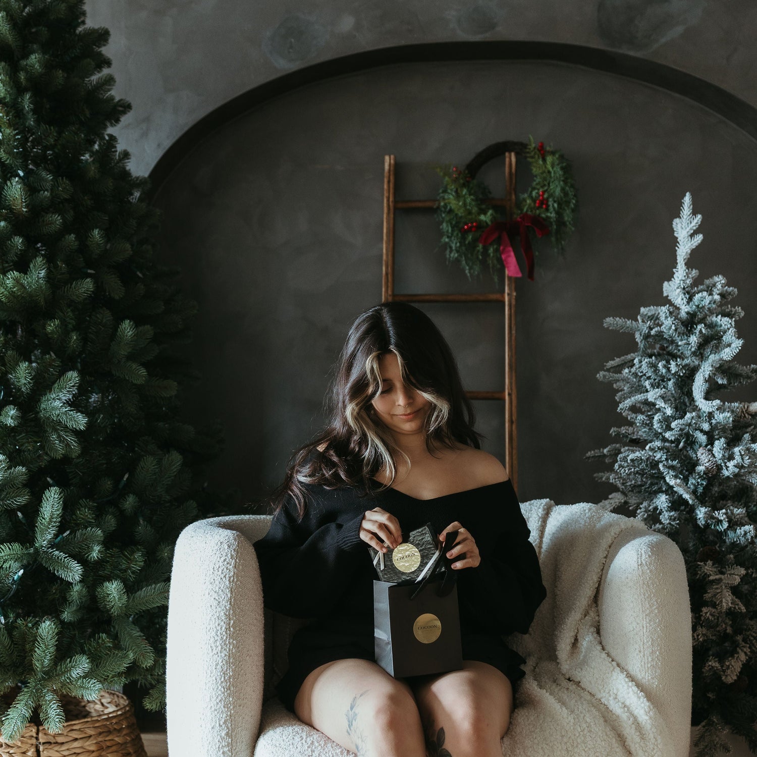 Woman sitting in a cozy room with Christmas decorations, holding a gift box.
