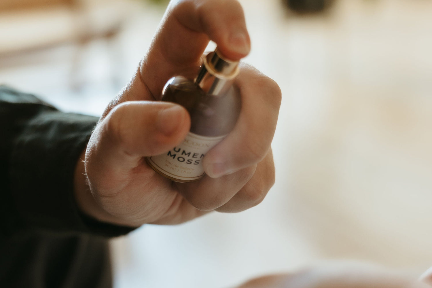 Hand holding a small bottle of perfume with a blurred background