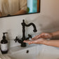 Person washing hands under a black faucet in a bathroom.