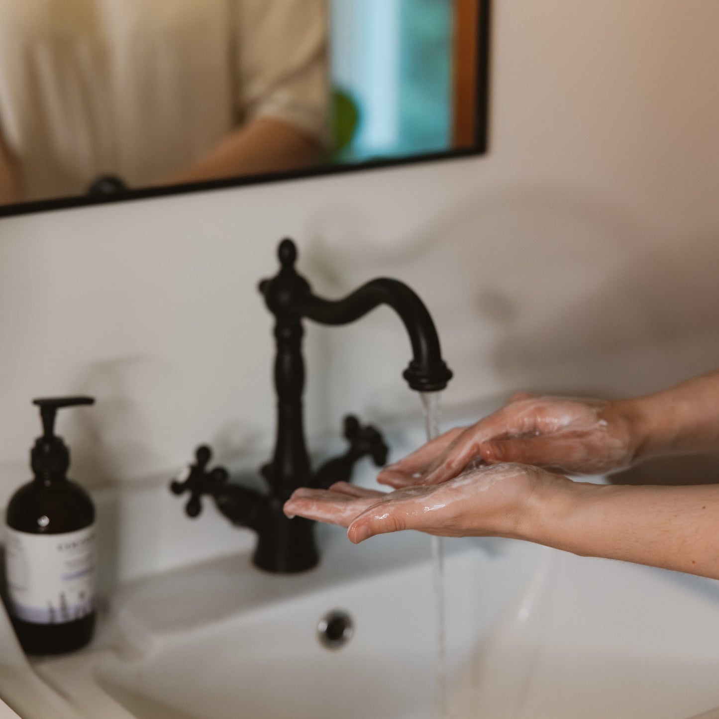 Person washing hands under a black faucet in a bathroom.