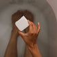 Person holding a bath cube above a bathtub with water running.