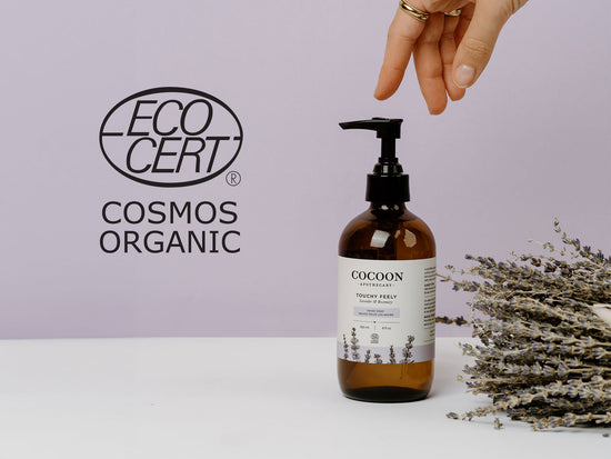 Cocoon bottle with lavender on a white surface and purple background, featuring EcoCert Cosmos Organic logo.