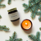 Candle and jar with 'Balsam Fir' label surrounded by pine branches on a light background