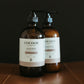 Two bottles of Cocoon Skincare on a brown surface with a dark background