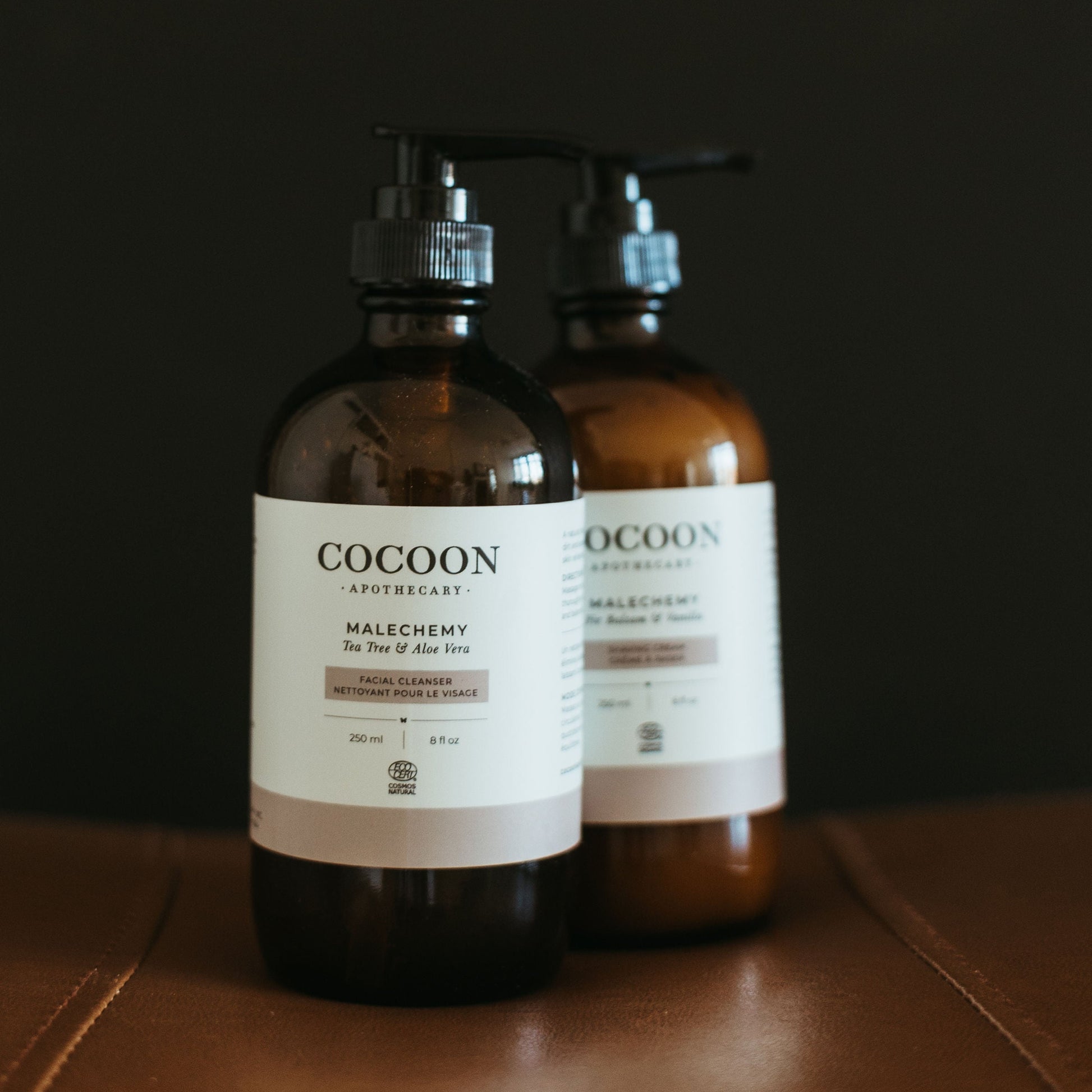 Two bottles of Cocoon Skincare on a brown surface with a dark background