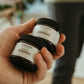 Hand holding two jars of Cocoon hair products with a blurred indoor background