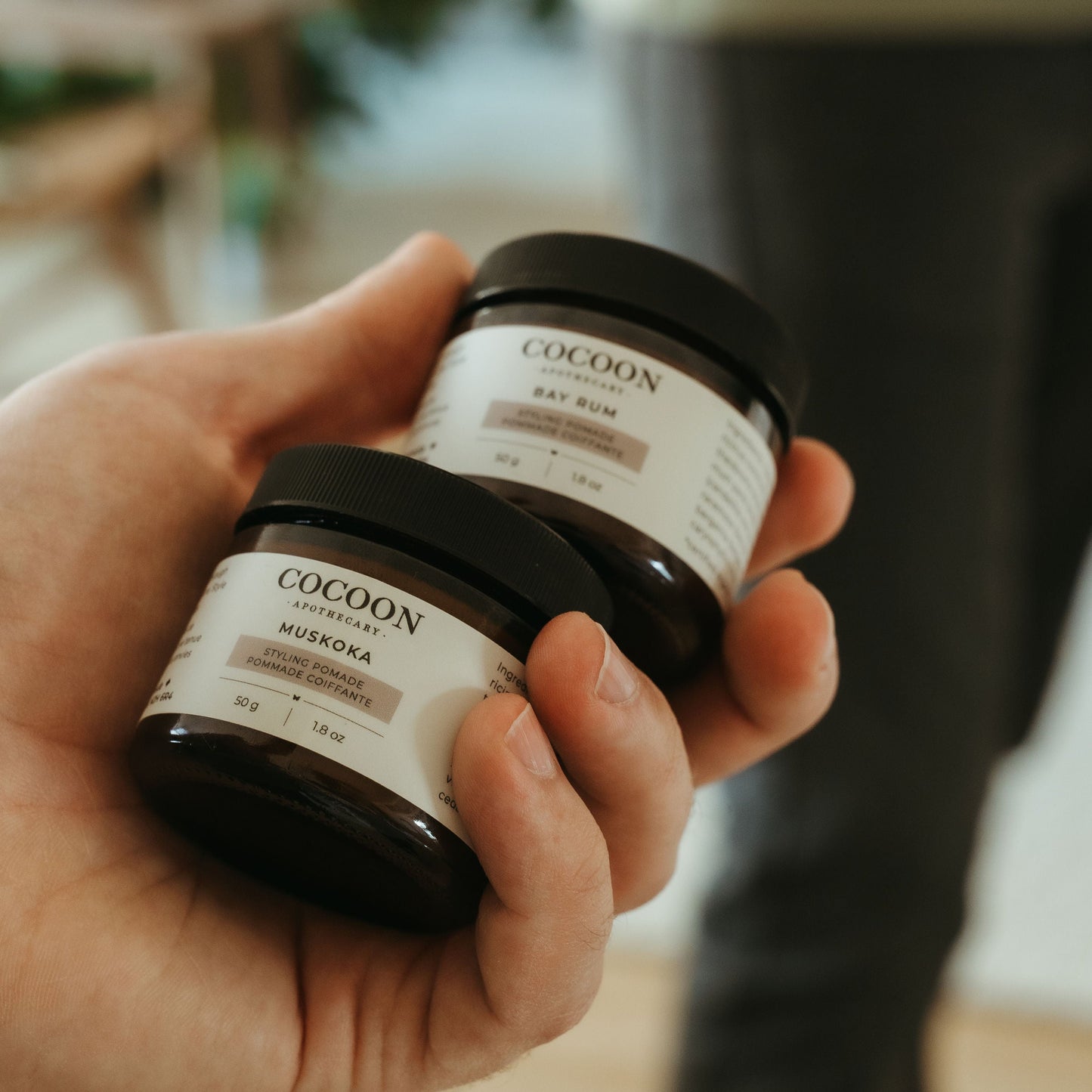 Hand holding two jars of Cocoon hair products with a blurred indoor background