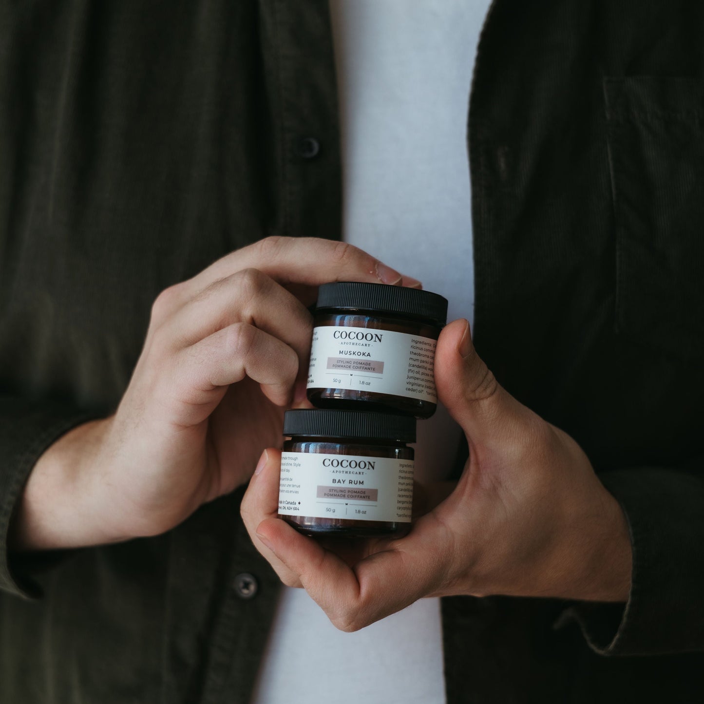 Person holding two small pomade jars with a dark background