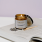 Cocoon Lavandin candle in a brown jar on an open book with lavender flowers.