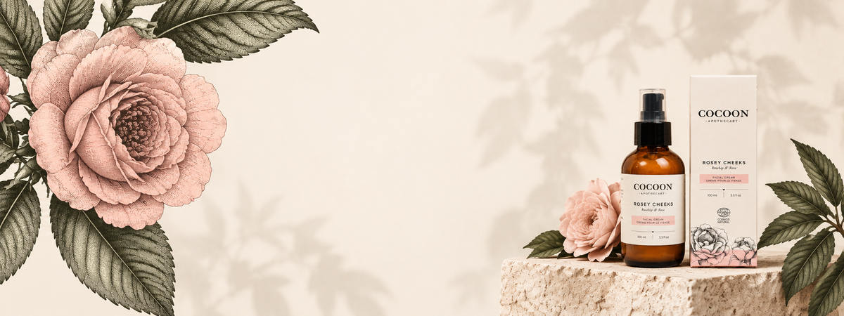 rosey cheeks packaging box displayed on a stone pedestal, styled with pink roses and green leaves against a warm beige background with leaf shadows.