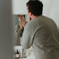 Man shaving in front of a bathroom mirror with toiletries on the sink.