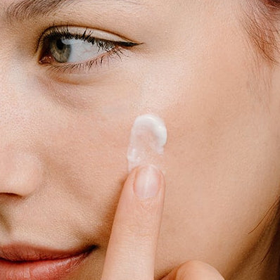 Woman applying a product from a Cocoon skincare bottle to her face.