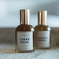 Two perfume bottles labeled 'Terre Noir' and 'Lumen Moss' on a marble surface with a blurred background.