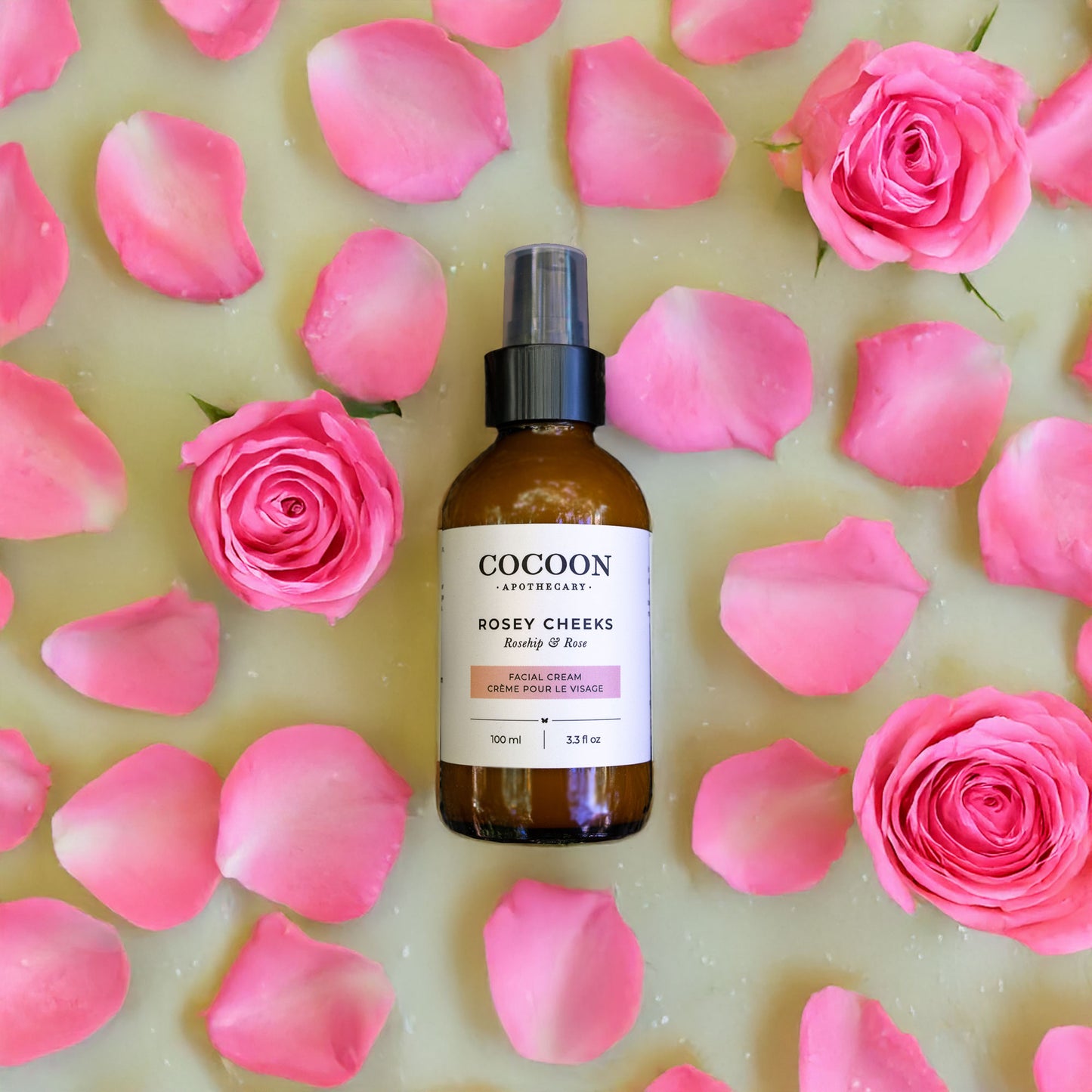 Cocoon Apothecary bottle of Rosey Cheeks product surrounded by pink roses and petals on a light background