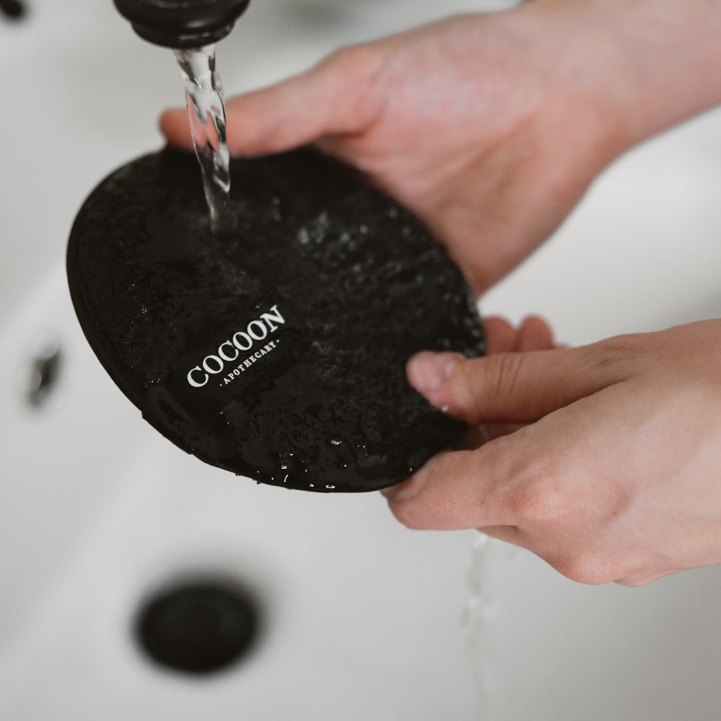 Person washing a black Cocoon sponge under running water.